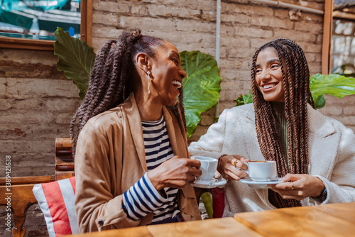 Two happy black women having coffee together in an outdoor cafe, laughing and enjoying. Mother and daughter.