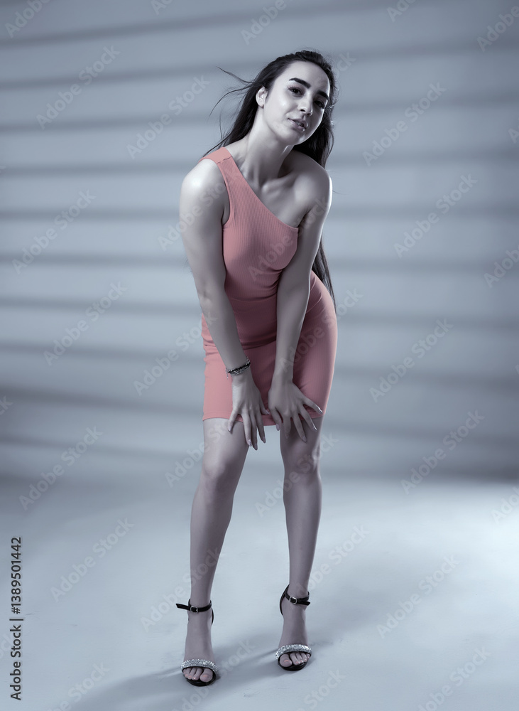 Fashion model in coral one-shoulder dress posing in studio.........