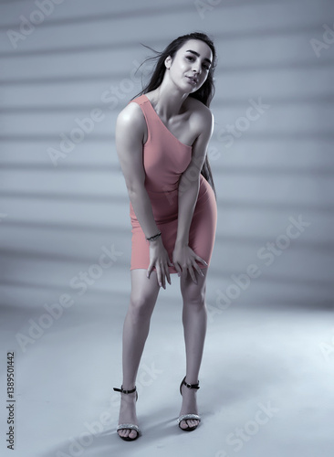 Fashion model in coral one-shoulder dress posing in studio.........