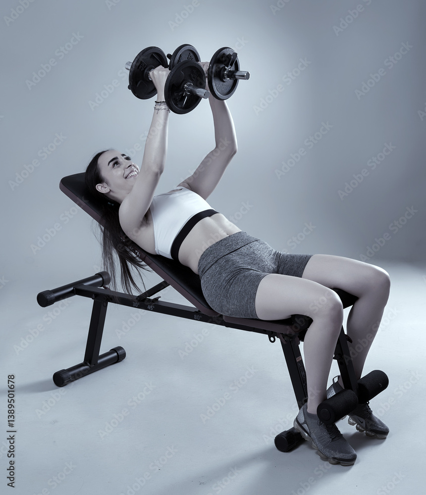 Athletic woman performing dumbbell bench press in studio.........