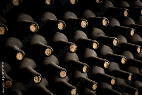 Rows of dust-covered wine bottles with corks intact are neatly stacked in a dimly lit cellar