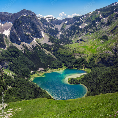 Trnovacko Lake, Montenegro, Durmitor National Park. Small mountain glacial romantic lake in shape of a heart, surrounded with snowy rocky peaks and green forests.