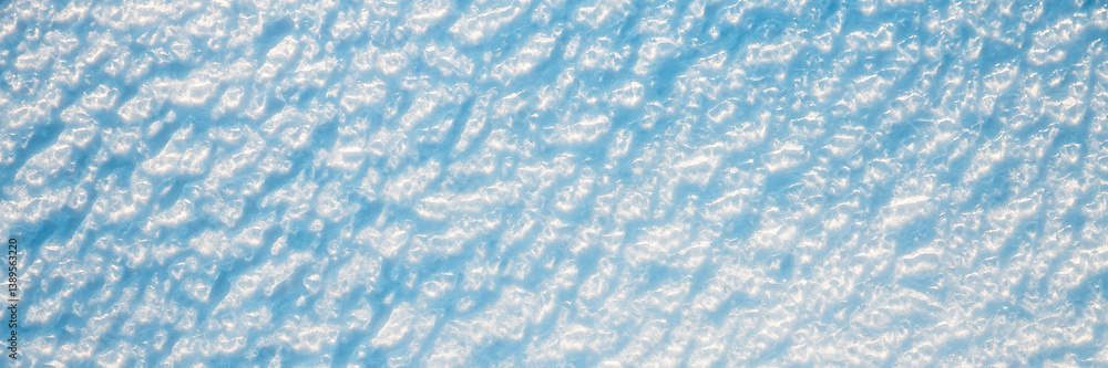 Beautiful winter background with snowy ground. Natural snow texture. Wind sculpted patterns on snow surface. Wide panoramic texture for background and design.