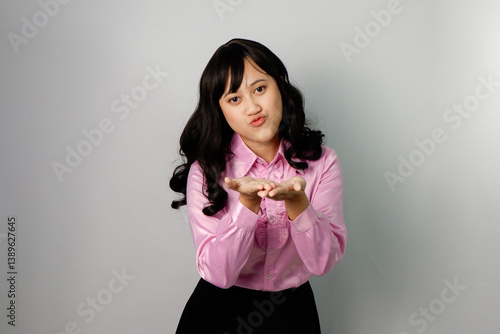 Asian woman with beautiful face wearing pink shirt showcasing kiss gesture from afar.