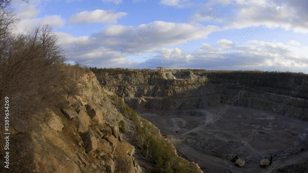 A rocky cliff with sparse trees and dry bushes under warm sunlight. At the top, an abandoned industrial structure stands among autumn foliage, creating a contrast between nature and human-made ruins. A rocky cliff with sparse trees and dry bushes under warm sunlight. At the top, an abandoned industrial structure stands among autumn foliage, creating a contrast between nature and human-made ruins.