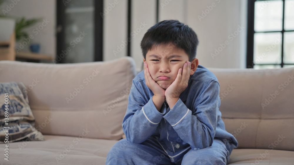 A young boy sitting on a couch with his hands covering his face, possibly feeling upset or overwhelmed