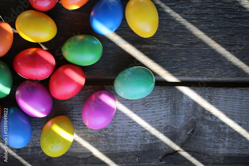 The Easter colorful eggs are lying on the wooden table. Sunrays are breaking through the wooden fence.