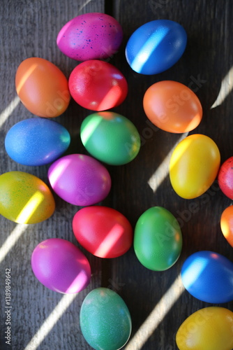 The Easter colorful eggs are lying on the wooden table. Sunrays are breaking through the wooden fence.