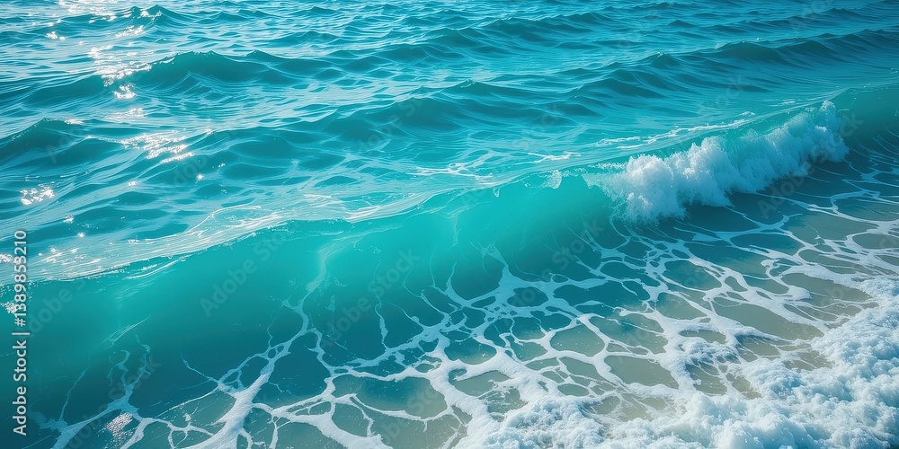 Fototapeta premium A powerful wave crashes onto the sandy shore, sending white foam spraying into the air. The vibrant blue ocean glistens under the sunlight, creating a serene yet dynamic scene.