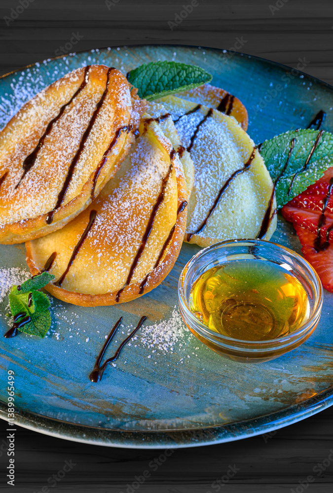 sweet pancakes with syrup, powdered sugar, honey and strawberries served on a blue plate
