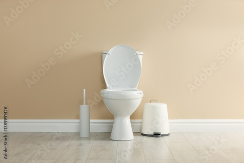 Foto Toilet bowl, brush and trash bin near beige wall in restroom