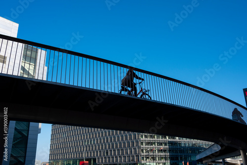 Silhouetted bike rider on curved bridge between buildings in Copenhagen, Denmark, symbolizing healthy transport, clean air and integrated urban cycling infrastructure.