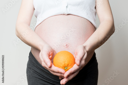 natural vitamins for pregnant women, fruits during pregnancy, orange in hand and pregnant belly