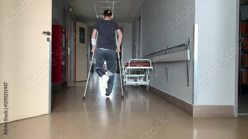 A man with a broken leg walks on crutches down a hospital corridor.