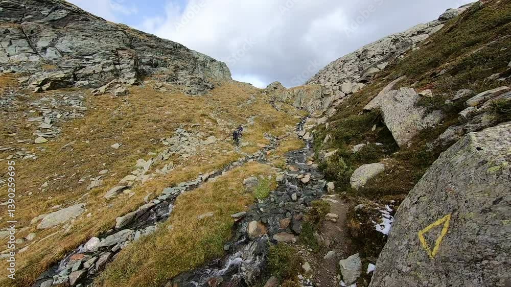 Two bikers navigate a rough, high-altitude trail carved into the mountainside, surrounded by jagged rocks and sweeping vistas. Two bikers navigate a rough, high-altitude trail carved into the mountainside, surrounded by jagged rocks and sweeping vistas.