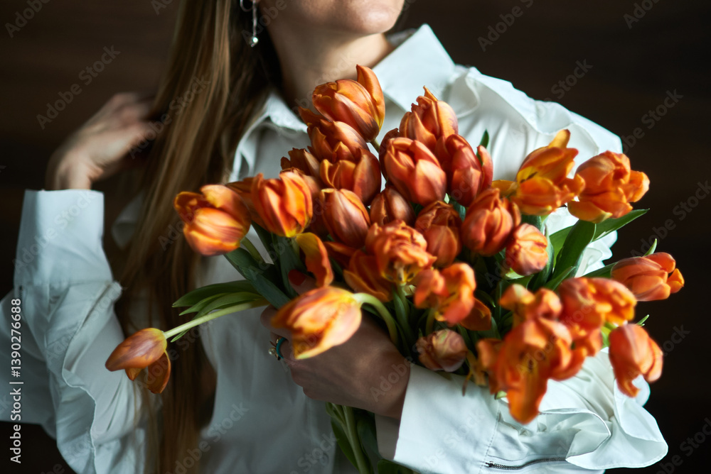 Woman holding vibrant bouquet of orange tulips in natural light, close-up with white blouse, floral elegance, springtime bloom concept