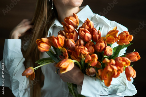 Obraz na płótnie Woman holding vibrant bouquet of orange tulips in natural light, close-up with white blouse, floral elegance, springtime bloom concept w salonie
