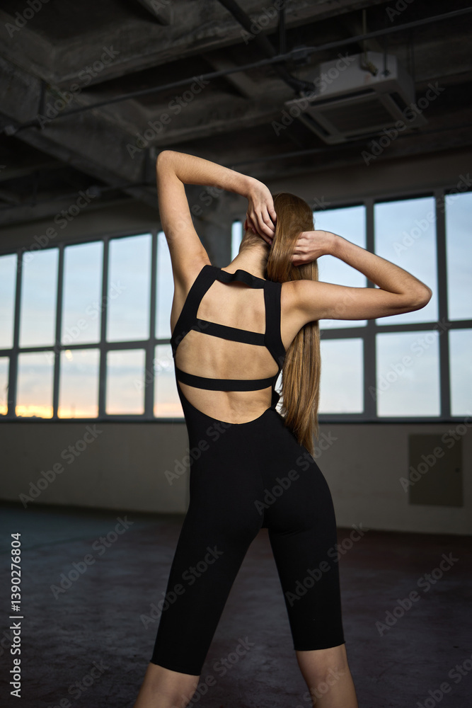 Athletic woman in stylish black workout jumpsuit showcasing fit posture in an indoor gym environment, graceful movement concept