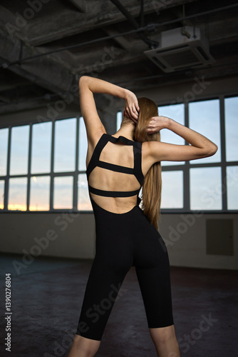 Obraz na płótnie Athletic woman in stylish black workout jumpsuit showcasing fit posture in an indoor gym environment, graceful movement concept w salonie