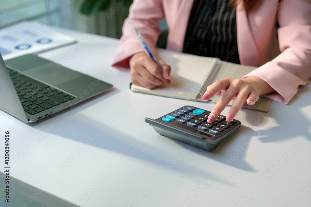 Businesswoman using calculator and writing notes in notebook while working with laptop in office Businesswoman using calculator and writing notes in notebook while working with laptop in office