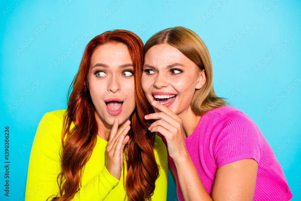 Vibrant young girlfriends sharing a secret in bright casual outfits against a turquoise background Vibrant young girlfriends sharing a secret in bright casual outfits against a turquoise background