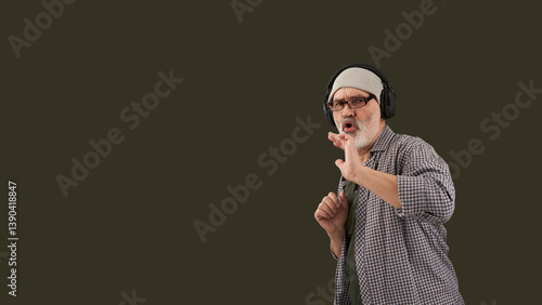 Obraz na płótnie An adult gray-haired and gray-bearded man listening to music on headphones. The background is dark green . Copy space. w salonie