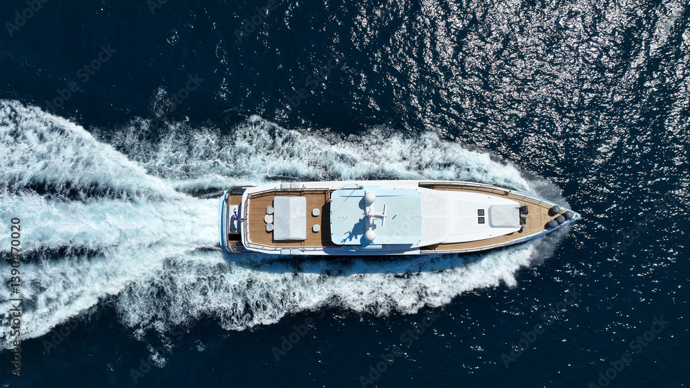 Aerial drone tracking photo of beautiful modern super yacht with wooden deck cruising in low speed deep blue Mediterranean sea