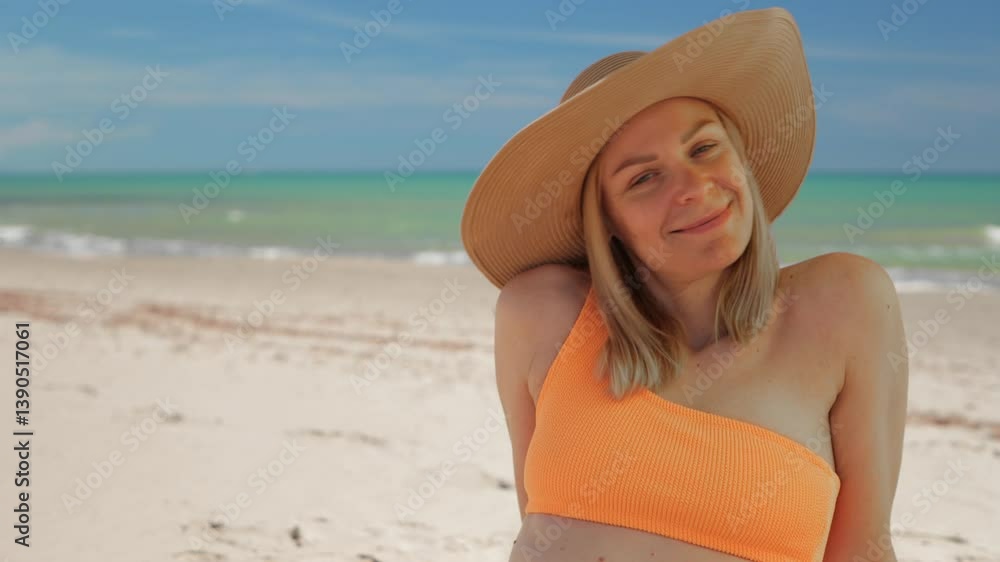 Blond woman sunbathing in orange bikini, sit by turquoise sea on white sandy beach, wearing straw hat and smiling Blond woman sunbathing in orange bikini, sit by turquoise sea on white sandy beach, wearing straw hat and smiling