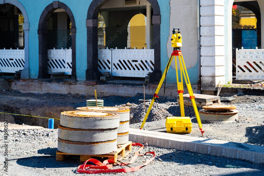 Urban construction site with survey tripod and stacked manhole covers