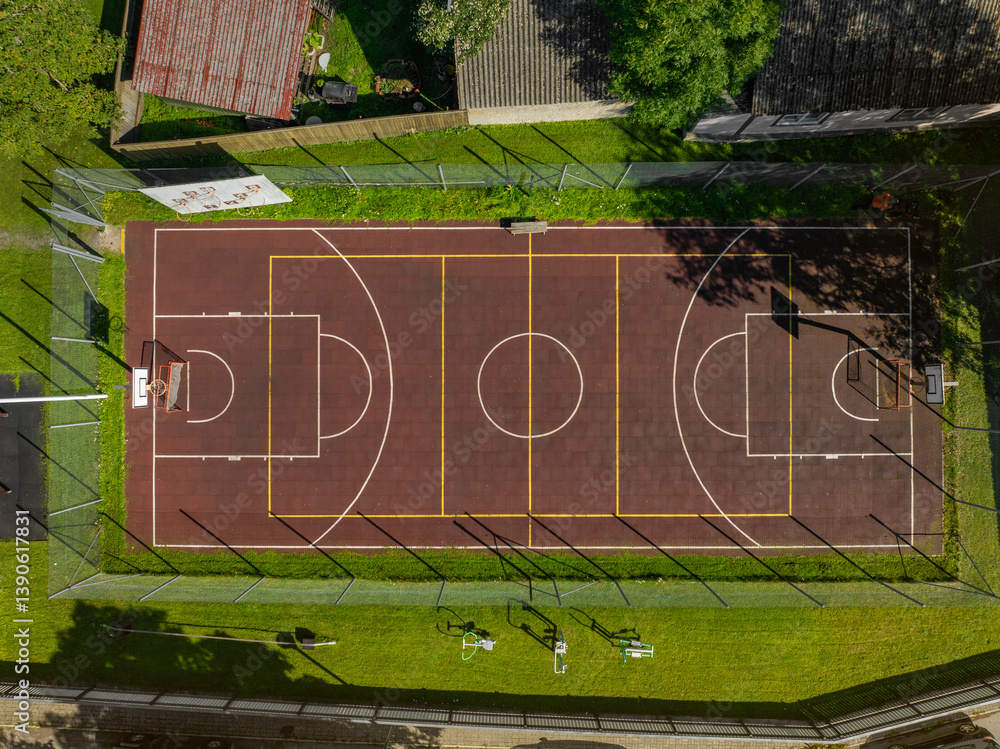 Obraz premium Aerial top down view of an outdoor basketball sports court of Haapsalu Primary School. The court is surrounded by a wire fence, green grass, and some gym equipment. Estonia