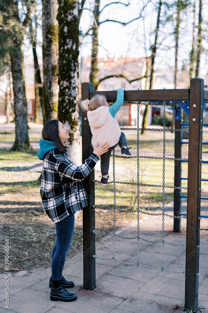 Smiling mother helping little girl climb chain ladder at playground Smiling mother helping little girl climb chain ladder at playground