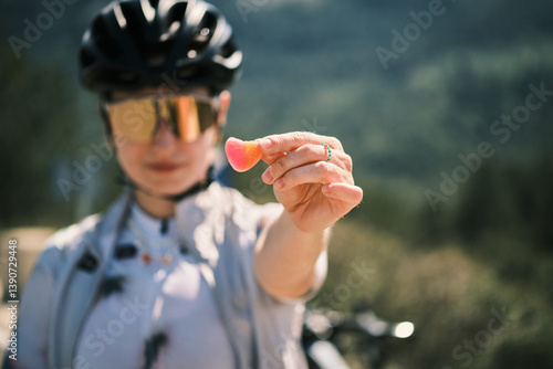 Close-up of a cyclist holding a vibrant, heart-shaped gummy candy. The blurry background emphasizes the bright colors of the treat and the cyclist's gear. Calpe,Alicante. Spain
