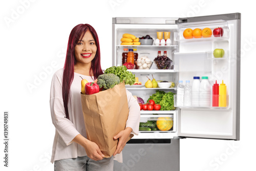 Foto Young asian woman with a grocery bag standing in front of a fridge