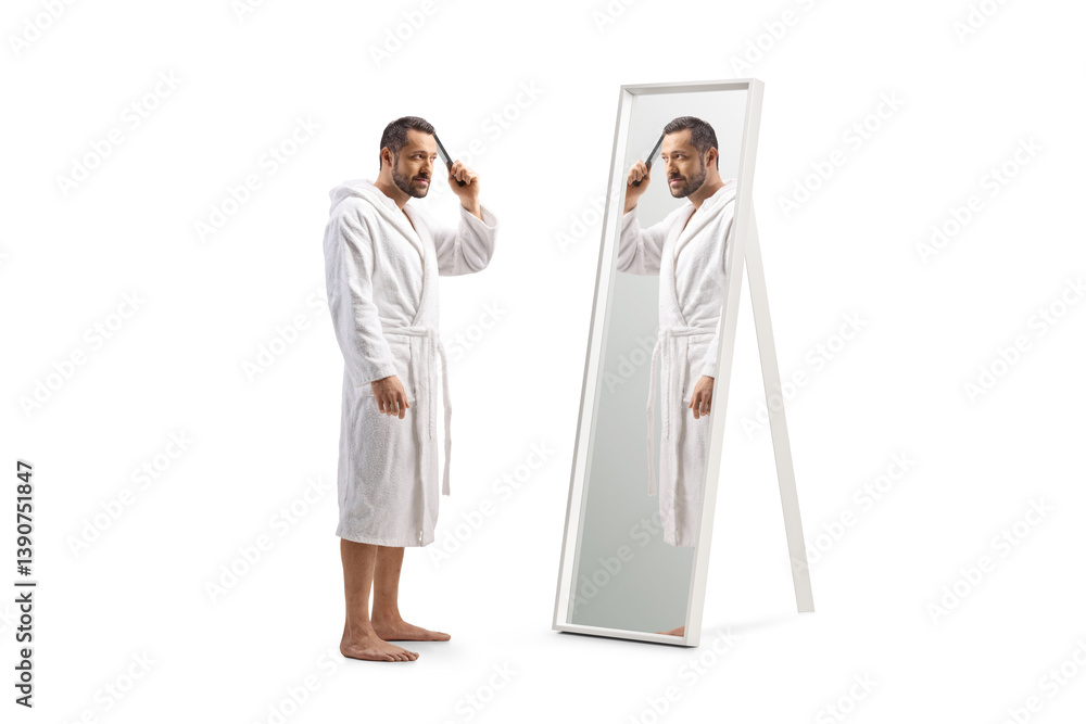 Man in a white bathrobe combing hair and looking at a mirror