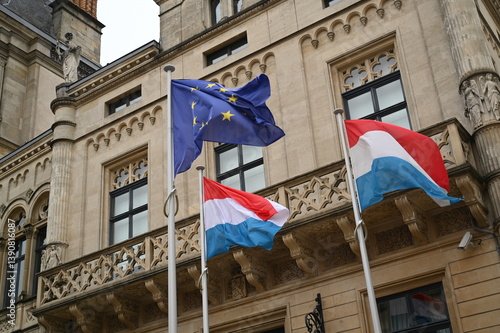 Flags of Luxembourg and the European Union waving near a historic building in Luxembourg City. Government, politics, diplomacy, and European unity concept.
