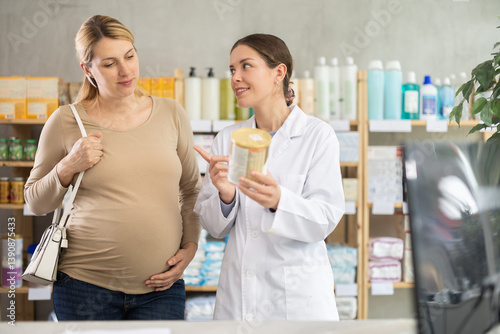 Obraz na płótnie Pregnant woman choose infant formula in pharmacy, examine packaging. Assortment of pharmacy children department. Girl pharmacist offer similar product, promotes product of European brand w salonie