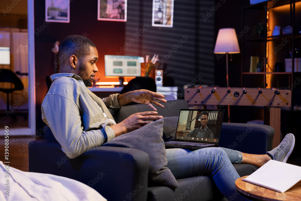 Obraz premium Focused black guy smiling and waving during a web conference in his living room, showcasing online discussion in a digital and wireless lifestyle. Conference speaker with attendees on call.