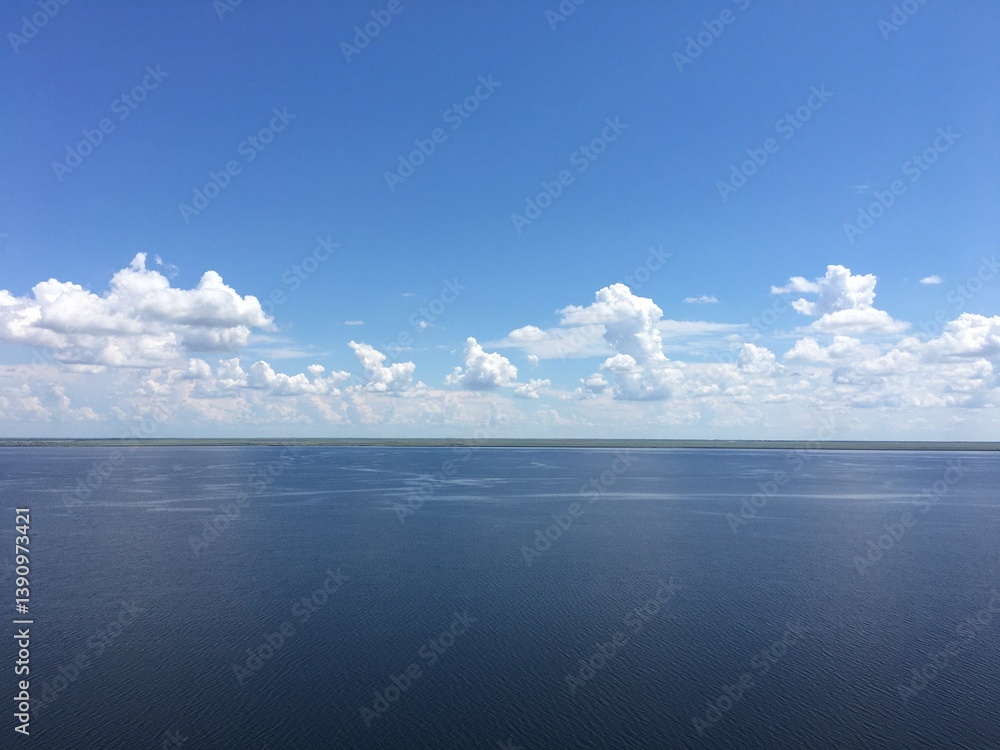 Fototapeta premium Clear blue sky with scattered clouds over calm lake horizon