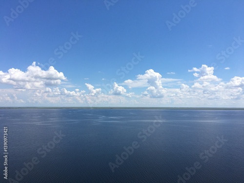 Konstfotografi Clear blue sky with scattered clouds over calm lake horizon