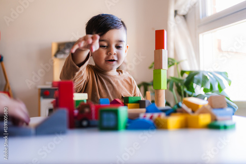 Young child building a tower with colorful wooden blocks, developing fine motor skills and creativity in a playful home environment