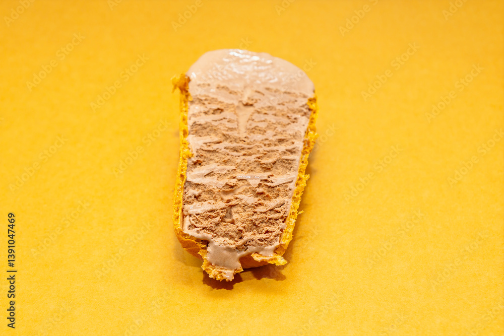 Slice of chocolate ice cream cake resting on smooth graham cracker crust with vibrant yellow background adding warmth to composition. Creamy texture of ice cream contrasts with crumbly golden crust