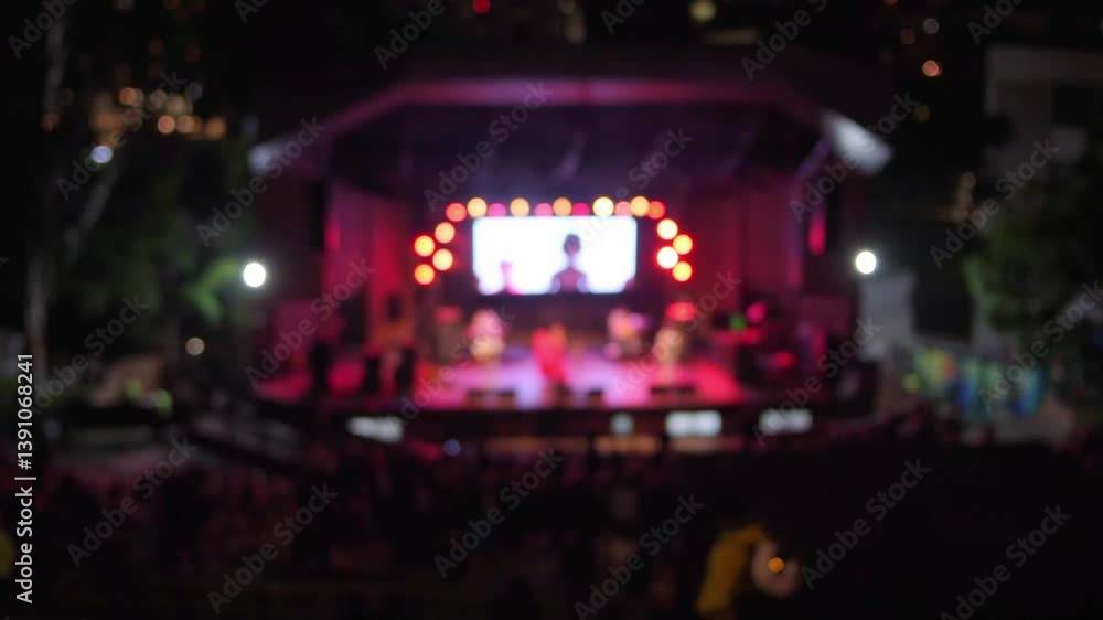 Defocused distant view of vibrant stage performance with colorful lighting during a lively event. Emphasizing community and entertainment.