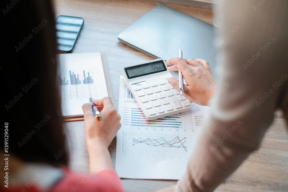 Professionals reviewing financial charts and using a calculator for data analysis in a contemporary office environment. Professionals reviewing financial charts and using a calculator for data analysis in a contemporary office environment.