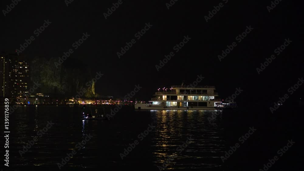 Ship Stationed in Bay at Night with Coastal City in Background Ship Stationed in Bay at Night with Coastal City in Background