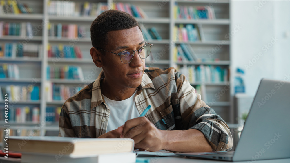 Fototapeta premium African American man working studying laptop desktop computer e-learning education male student copying writing notebook looking monitor preparing exam guy library technology knowledge college diploma