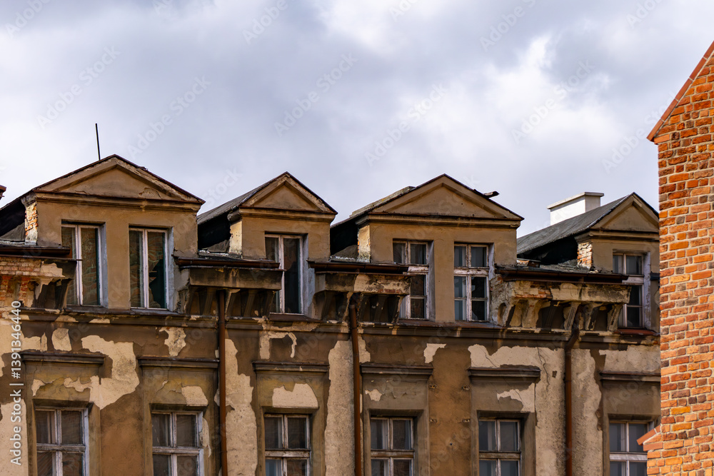 Obraz premium An old tenement house with visible signs of the passage of time. Falling plaster, damaged cornices and neglected windows. The building is in a classic style with triangular pediments above the attic w