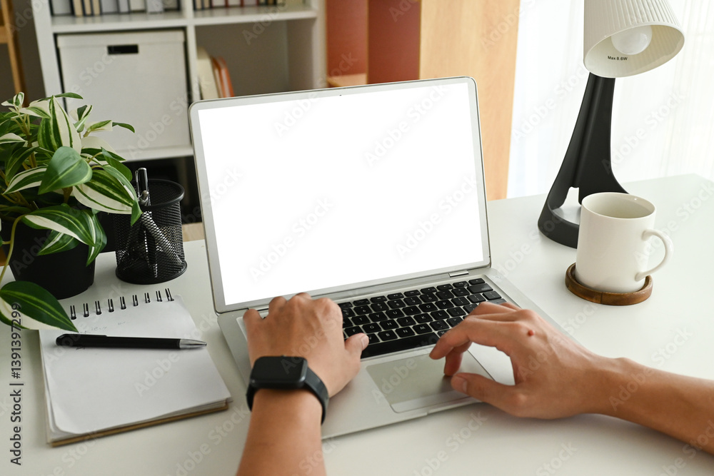 A person is typing on a laptop computer with a black pen and a notebook on the desk. The laptop screen is blank.