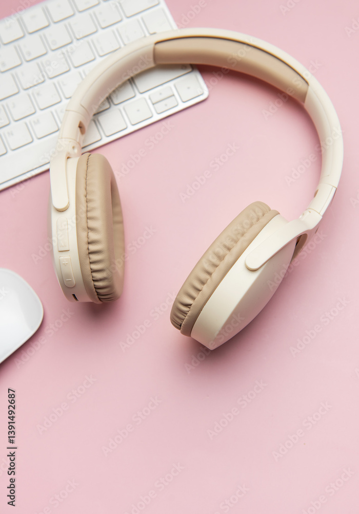 Wireless headphones, keyboard and mouse lying on pink table