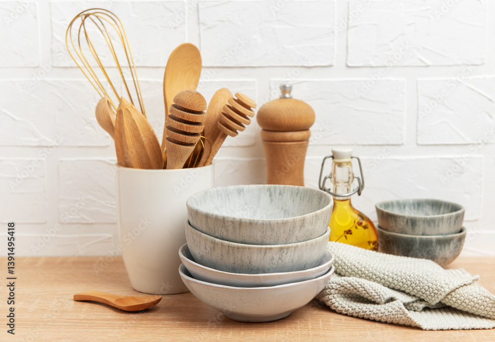 Kitchen utensils, bowls and ingredients resting on wooden countertop by white brick wall