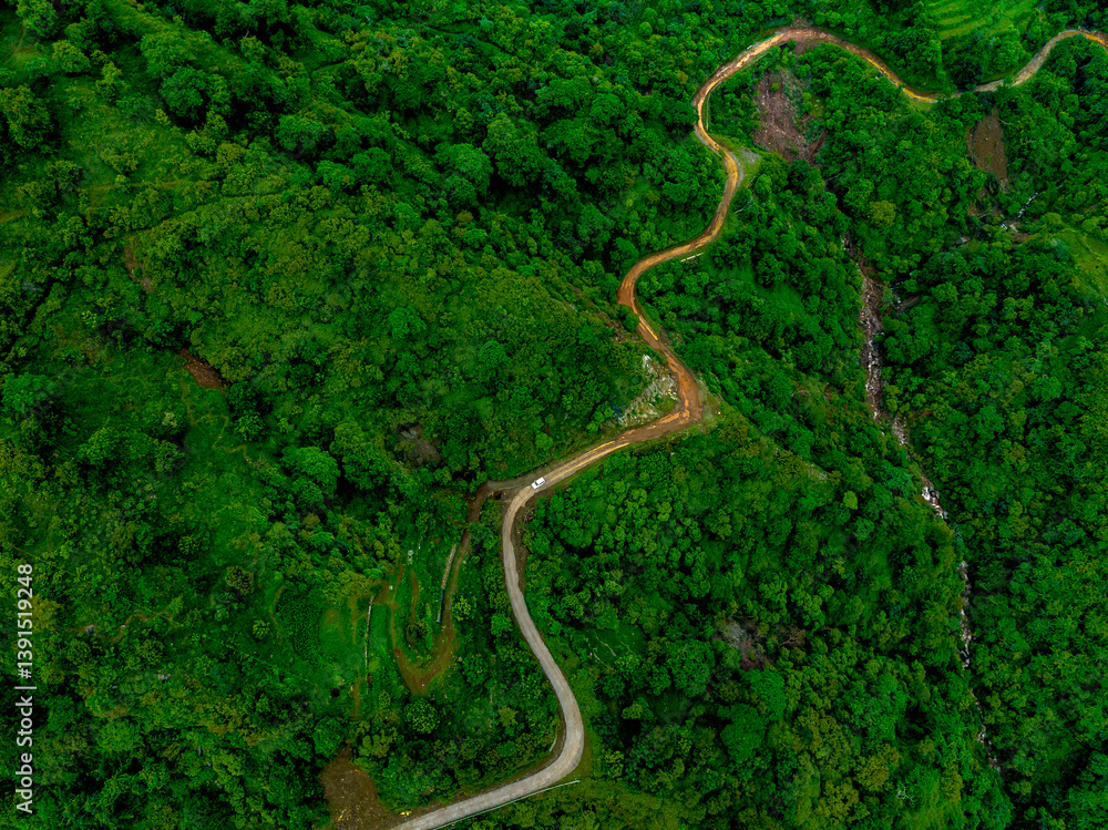 Aerial view of a muddy mountain road cutting through lush green hills during the monsoon season — showcasing the natural beauty of the rainy season in the mountains Aerial view of a muddy mountain road cutting through lush green hills during the monsoon season — showcasing the natural beauty of the rainy season in the mountains